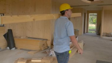 Genç marangoz modern CLT evinde uzun tahta bir kalas taşıyor.