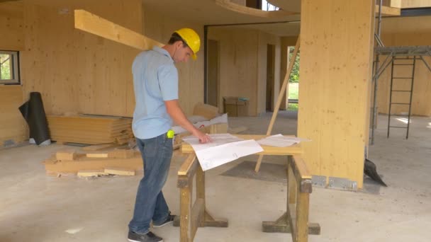 STÄNGA UPP: Man tittar på planritningar innan man bär en lång bräda över huset — Stockvideo