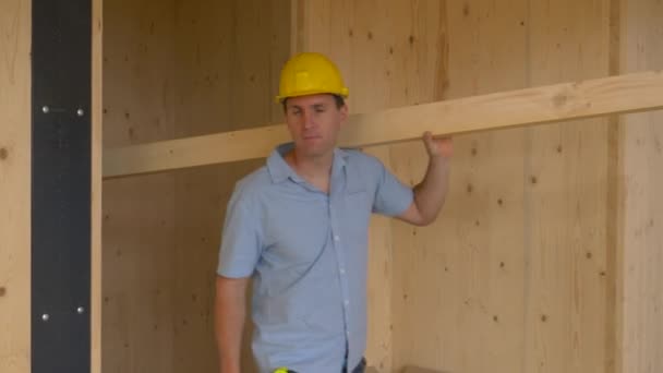 Sluiten omhoog: Werknemer met een lange plank kijkt rond het prachtige CLT huis. — Stockvideo