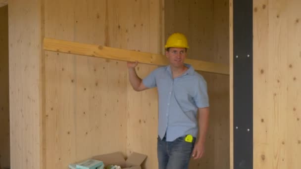 FECHAR UP: Carpinteiro feliz carregando uma prancha longa olha ao redor da casa CLT. — Vídeo de Stock