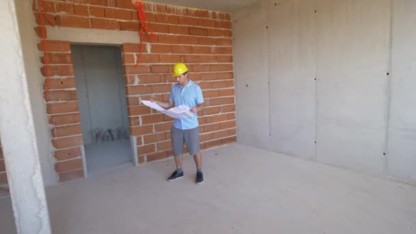 SLOW MOTION: Kaukasisk man bär en hård hatt inspekterar hus under uppbyggnad — Stockvideo