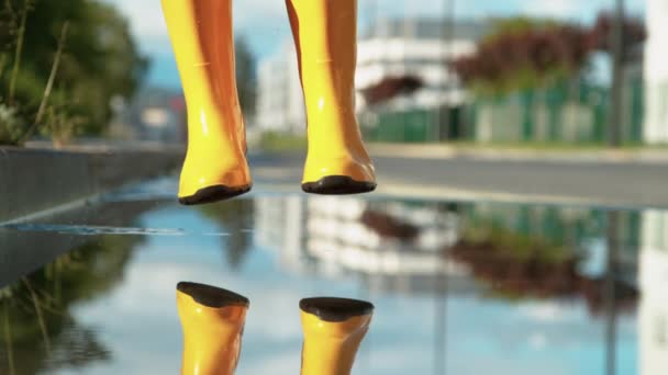 CLOSE UP Nerozpoznatelná dívka ve žlutých gumových botách skočí do skleněné louže — Stock video