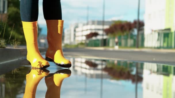 Uzavřete nahoru Žena v dešťových botách skočí z okraje chodníku do kaluže — Stock video
