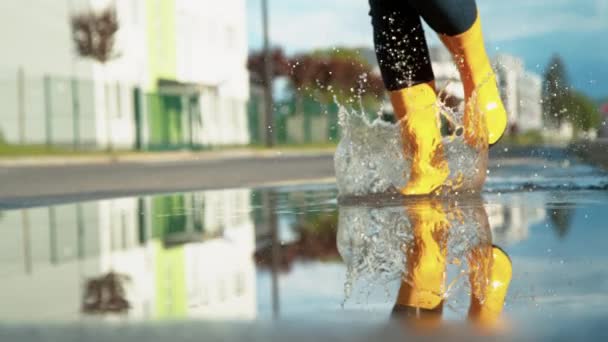 CLOSE UP: Filmisk skud af pige løber på tværs af en klar vandpyt efter regnvejr. – Stock-video