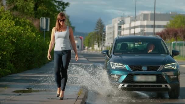 Řidič zaveze její auto do kaluže, stříkající vodu na chodci. — Stock video