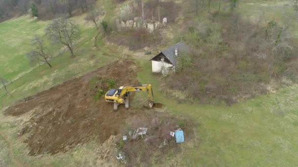 DRONE: Flyger ovanför en Caterpillar grävmaskin som gräver ett hål på landsbygden. — Stockvideo
