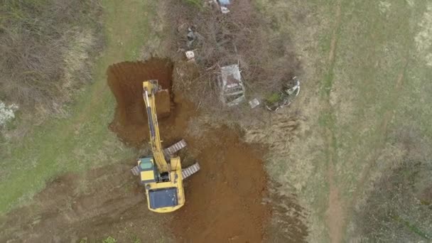 TOP DOWN: Volare sopra un escavatore giallo scavando una buca in campagna — Video Stock