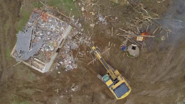 TOP DOWN: El operador de la excavadora ayuda al trabajador a quemar madera vieja cerca de una casa en descomposición . — Vídeo de stock