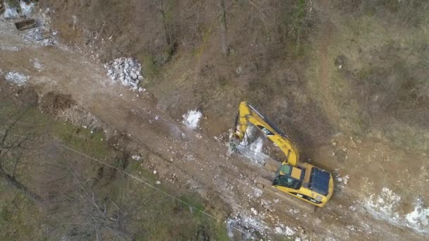 AERIAL: Caterpillar-grävmaskinen krossar stenar under vägarbeten på landsbygden — Stockvideo