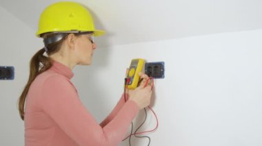 Genç bayan elektrikçi voltmetre kullanarak iki prizi kontrol ediyor..