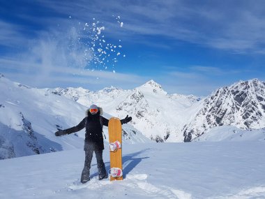 Oyuncu kadın snowboardcu bir avuç taze karı havaya fırlatıyor..