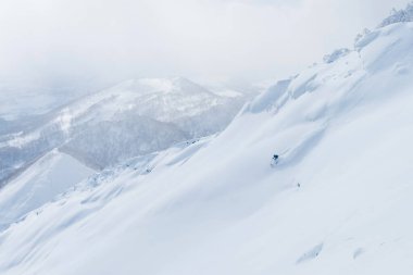 AERIAL: Man shredding the snowy mountain terrain while on fun ski trip in Japan. clipart