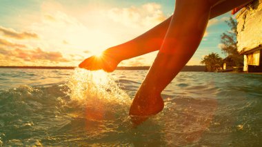 Güneşli bir sabahta çıplak ayakla su sıçratan dişi turist..