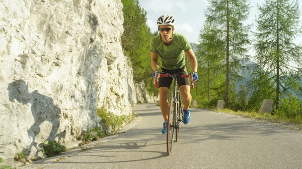 Młody rowerzysta szosowy pedałuje stromą górską drogą w słoneczny letni dzień. — Zdjęcie stockowe