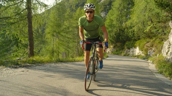 MOCIÓN LENTA: Hombre atlético caucásico pedaleando su bicicleta de carretera por una colina empinada . —  Fotos de Stock