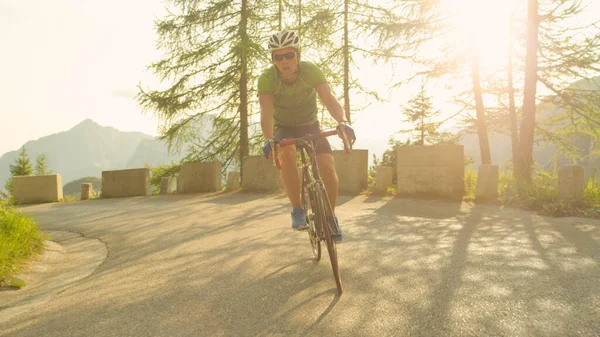 Młody mężczyzna droga rowerzysta zabawy pedałowanie w górę strome asfalt droga w słoneczny dzień — Zdjęcie stockowe