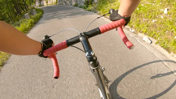 POV: Hombre montando una bicicleta de carretera por un camino empinado de asfalto corriendo por el bosque . —  Fotos de Stock