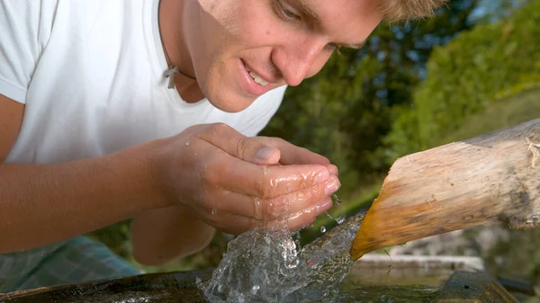 CHIUDI: Gioioso turista maschio rinfrescante lavando il viso con acqua corrente. — Foto Stock