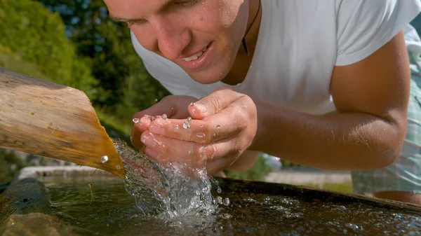 FECHAR-SE: Homem caucasiano sorridente levanta um punhado de água vítrea para beber . — Fotografia de Stock