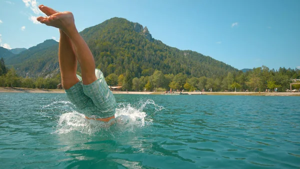 FERMER : Touriste masculin ludique saute dans le lac froid par une chaude journée d'été. — Photo