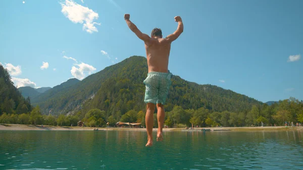 FERMER : Un touriste masculin insouciant saute les jambes en premier dans le lac d'émeraude froid. — Photo