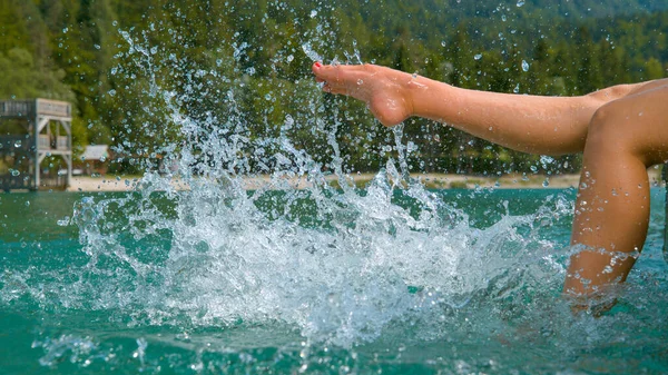 閉じる:認識できない遊び心のある女の子が蹴ったり、エメラルド湖の水を飛び散ったり. — ストック写真