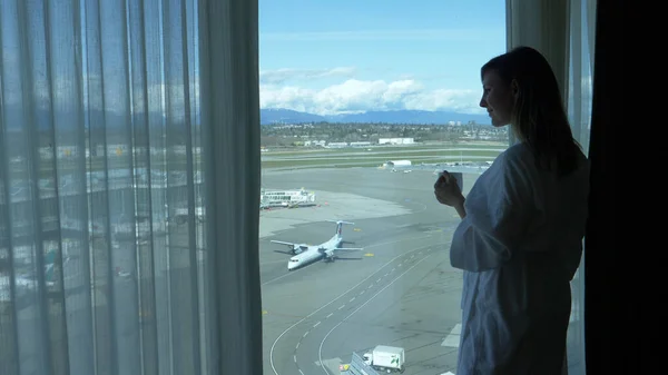 FERMER : Une jeune femme souriante tient une tasse de thé tout en observant l'aéroport. — Photo