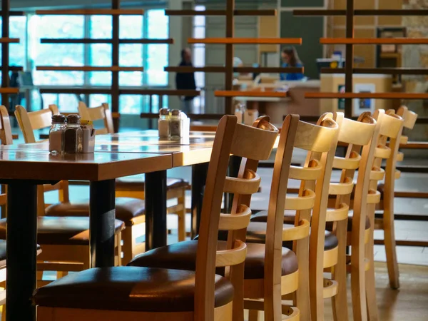 ZAMKNIJ: Puste drewniane krzesła są ustawione wokół stołów w restauracji na lotnisku. — Zdjęcie stockowe