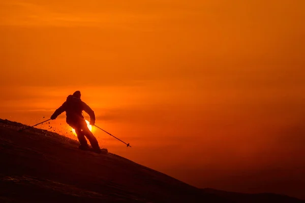 SILHOUETTE: nierozpoznawalny narciarz rozdrabniający świeży nietknięty śnieg o zachodzie słońca. — Zdjęcie stockowe