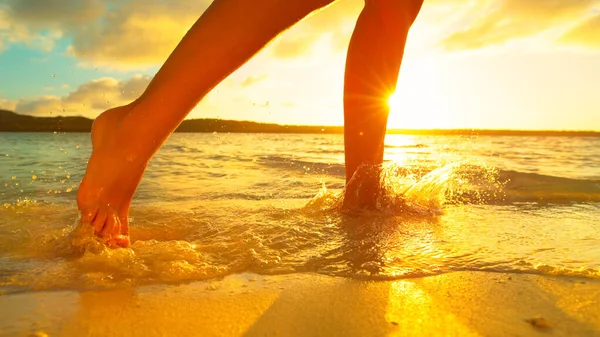 LENS FLARE: La ragazza spruzza l'acqua cristallina del mare mentre corre lungo la riva sabbiosa. — Foto Stock