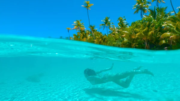 HALF HALF: Żeńska turystka nurkująca wzdłuż piaszczystej plaży w dziewiczej oceanicznej wodzie — Zdjęcie stockowe