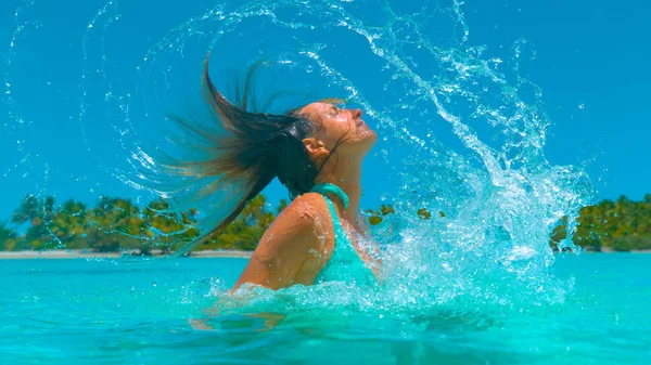 Bezárás: nő nyaralás ostorozza nedves haját vissza, és permetezi üveges víz — Stock Fotó