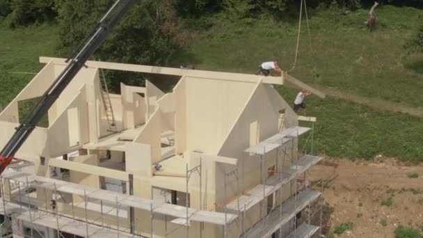 Los trabajadores de AERIAL se acercan para atrapar vigas de madera mientras están en el techo de la casa sin terminar — Vídeos de Stock