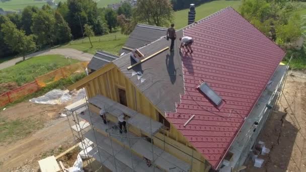 AERIAL Volando cerca de una casa en construcción mientras los trabajadores colocan láminas de techo de hojalata — Vídeos de Stock