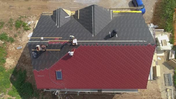 TOP DOWN: Fliegen über einem Haus, das im Bau ist, während Arbeiter Dachplatten legen — Stockvideo