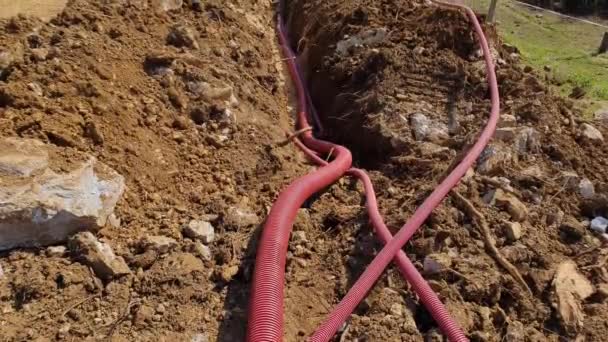 FECHAR UP: Condutos utilitários vermelhos correm ao longo da trincheira profunda perto do canteiro de obras — Vídeo de Stock