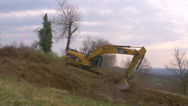 Caterpillar εκσκαφέας σκάβει μέχρι ξηρά κλαδιά από λιβάδι στη σλοβενική ύπαιθρο — Αρχείο Βίντεο