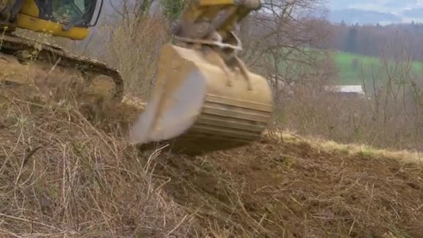 Kbelík na bagry škrábe větve stromů ze strany travnatého kopce.. — Stock video