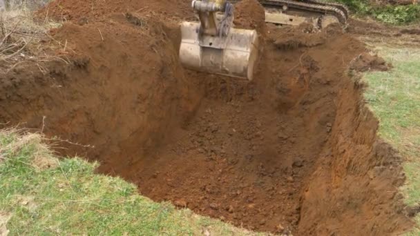 CERRAR: La excavadora amarilla cava un agujero profundo en medio de un prado. — Vídeo de stock