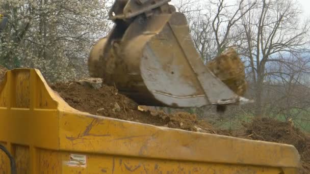 CERRAR El camión se aleja después de que la excavadora descarga un cubo lleno de tierra en la parte posterior — Vídeos de Stock
