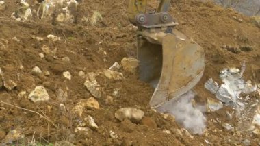 Metal kazıcı kovası inşaat alanının yakınındaki toprak ve kayaları topluyor.