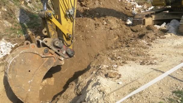 CLOSE UP: Gelber Bagger hebt tiefen Graben in der Nähe einer Baustelle aus. — Stockvideo