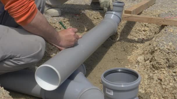 CERRAR: Constructor irreconocible marca un tubo de aguas residuales de plástico con un lápiz. — Vídeos de Stock