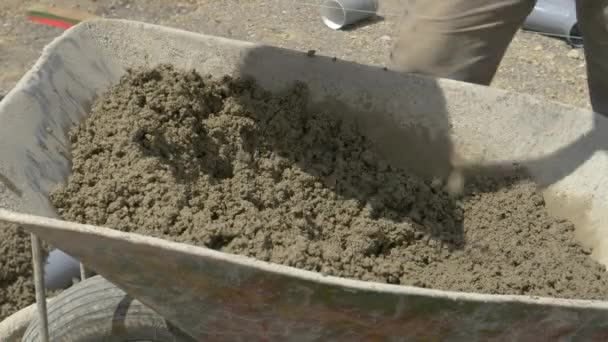 CLOSE UP: Bouwer schept een schop vol nat beton uit een kruiwagen. — Stockvideo
