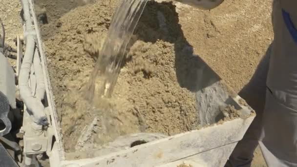 闭合：承包商将一桶水倒入搅拌机中的混凝土混合物中. — 图库视频影像
