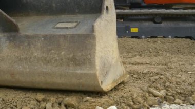 Buldozer operatörü, büyük bir kepçeyle sert ve ıslak çakıl tabakasını dümdüz ediyor.