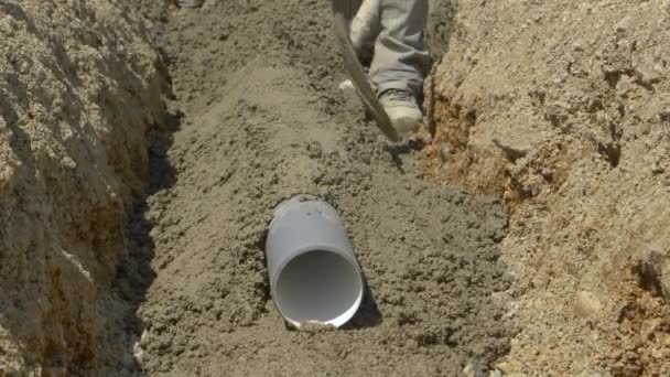 FERMER : Le tuyau en plastique posé au fond d'une tranchée est recouvert de béton frais — Video