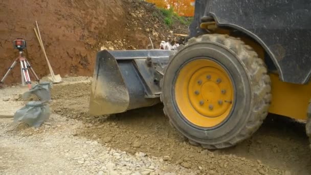 CERRAR: El operador de la excavadora utiliza el cucharón delantero para nivelar una capa de grava húmeda — Vídeo de stock