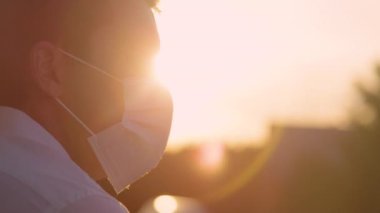 Milenyum erkeği altın ışıklı doğaya bakarken maske takar..