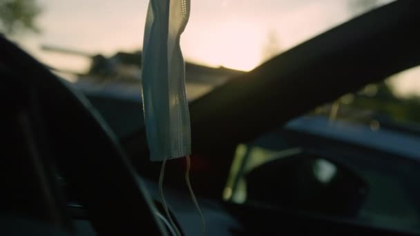 CERRAR: Los rayos de sol dorados de la mañana brillan en la mascarilla médica que cuelga dentro de un coche — Vídeo de stock